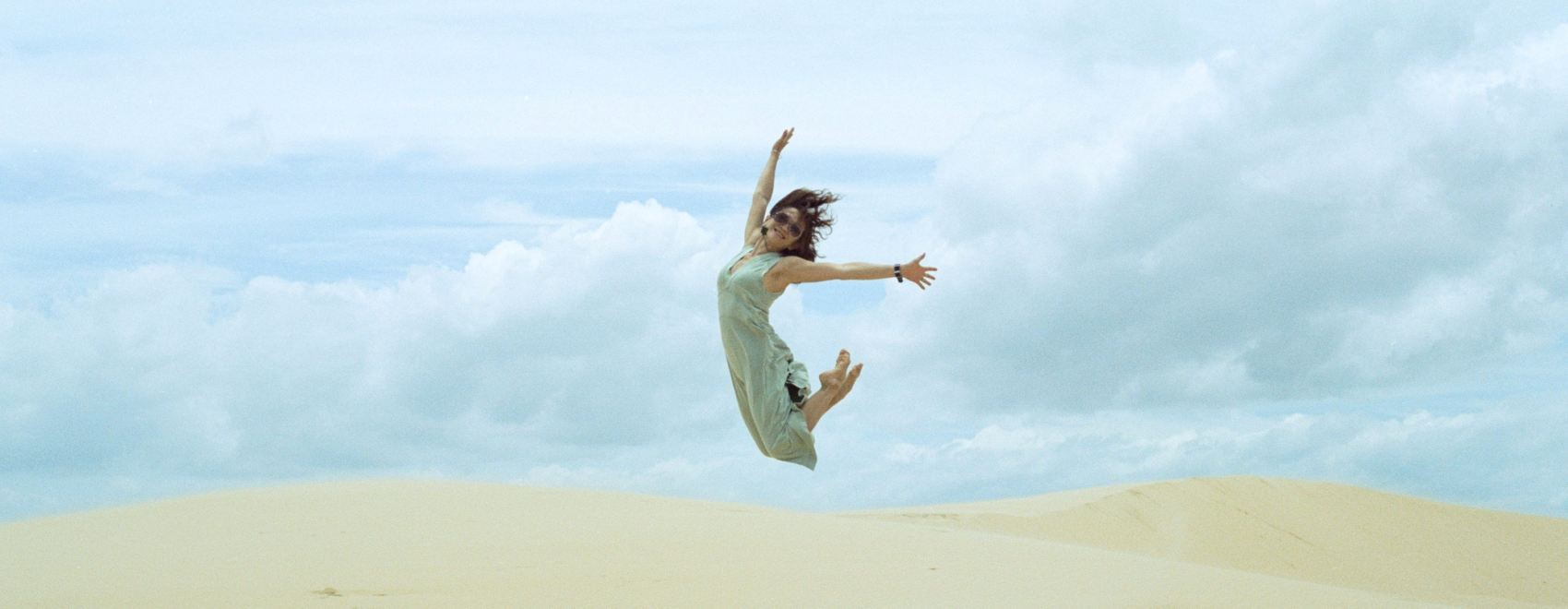 Woman jumps toward the sky in a white dress in a desert setting.